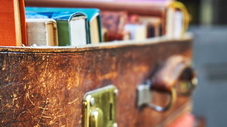 Close-up of an open vintage leather suitcase packed with books.