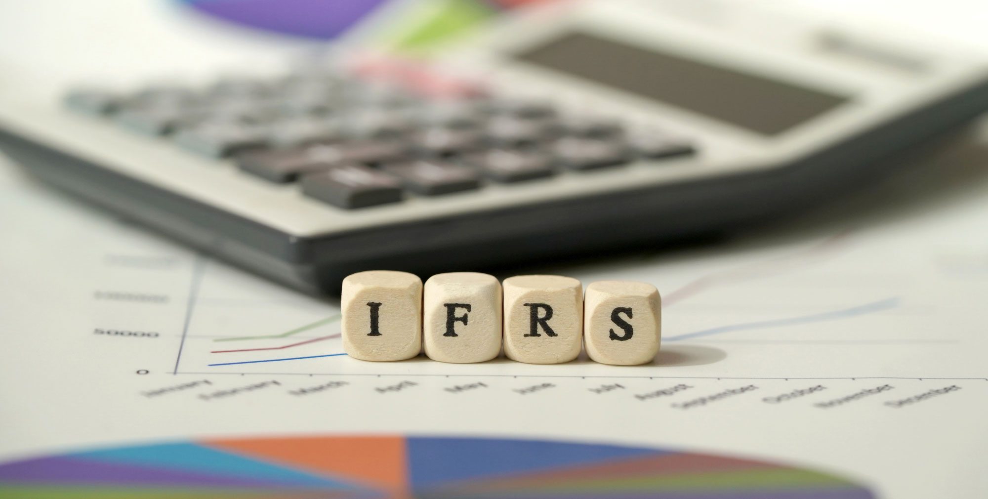 Wooden letter cubes spelling IFRS on a financial chart, with a calculator in the background.