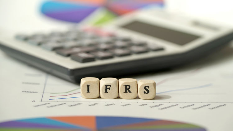 Wooden letter cubes spelling IFRS on a financial chart, with a calculator in the background.